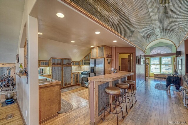1120 County Road 322, Westcliffe, CO 81252 - kitchen featuring vaulted ceiling, stainless steel appliances, light wood finished floors, brown cabinets, and a kitchen breakfast bar