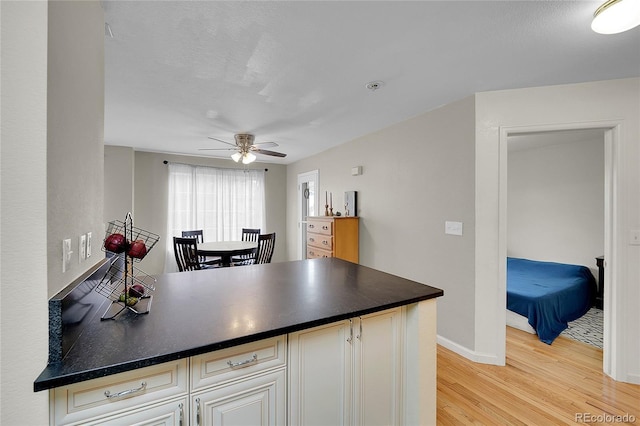 1308 S Danube Way Unit 102, Aurora, CO 80017 - kitchen with light wood-type flooring, ceiling fan, dark countertops, baseboards, and a peninsula