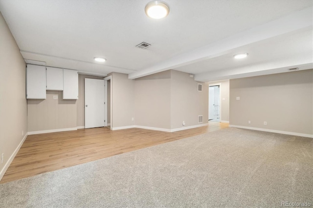 finished below grade area with light wood-type flooring, visible vents, and light carpet