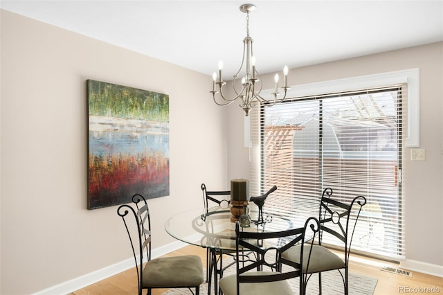 dining area with light wood finished floors, an inviting chandelier, visible vents, and baseboards