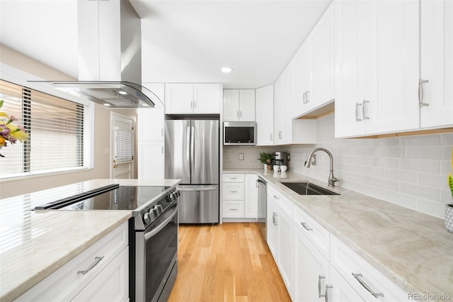 kitchen with light stone counters, appliances with stainless steel finishes, white cabinetry, a sink, and island range hood