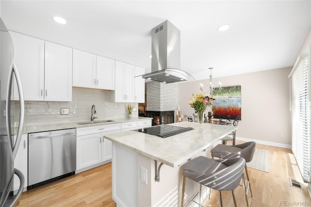 kitchen with island range hood, a sink, white cabinetry, appliances with stainless steel finishes, and pendant lighting