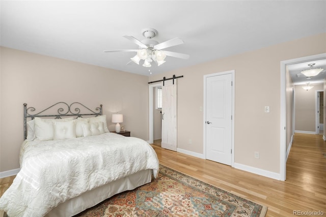 bedroom featuring a ceiling fan, wood finished floors, baseboards, and a barn door