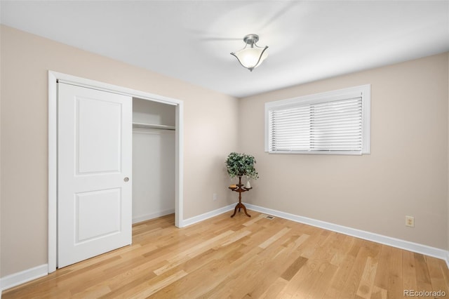 unfurnished bedroom featuring light wood-type flooring, a closet, and baseboards