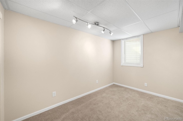 carpeted empty room featuring track lighting, a paneled ceiling, and baseboards