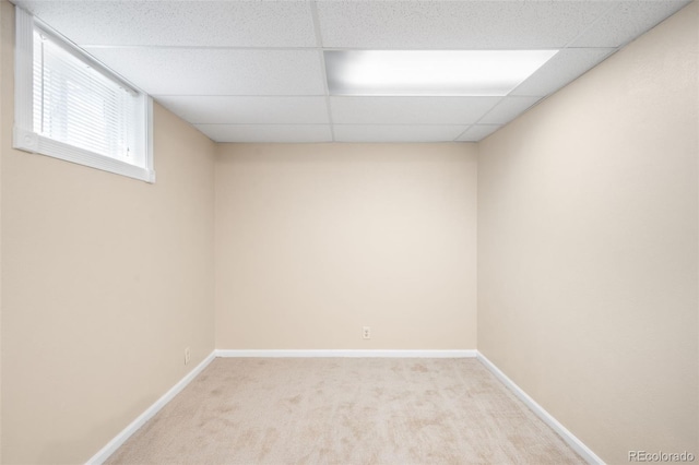 interior space featuring a paneled ceiling, light carpet, and baseboards