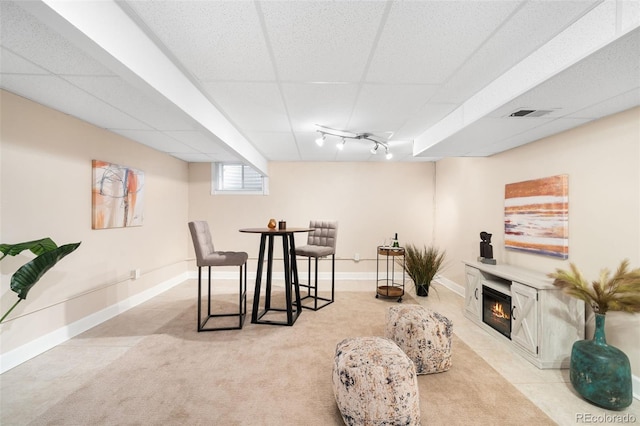 interior space featuring a paneled ceiling, visible vents, baseboards, a glass covered fireplace, and track lighting