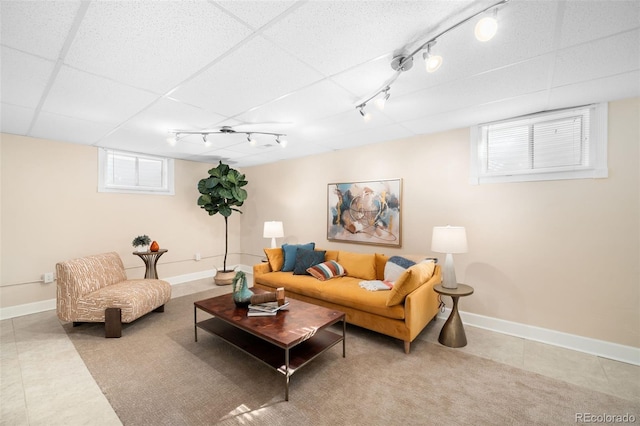 living room with light tile patterned flooring, a drop ceiling, and baseboards