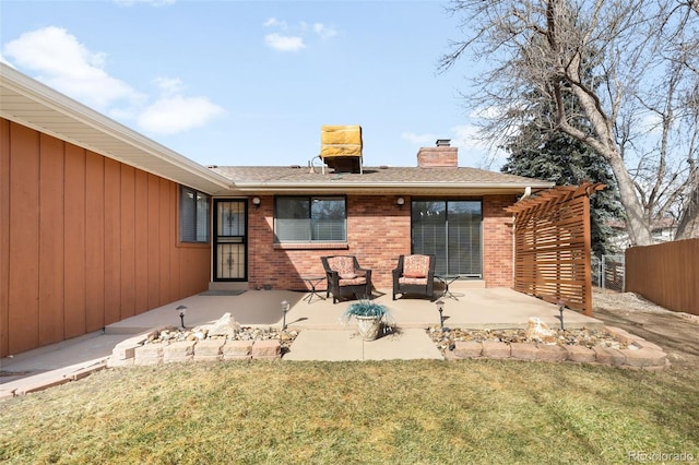 back of property with a lawn, a chimney, fence, a patio area, and brick siding