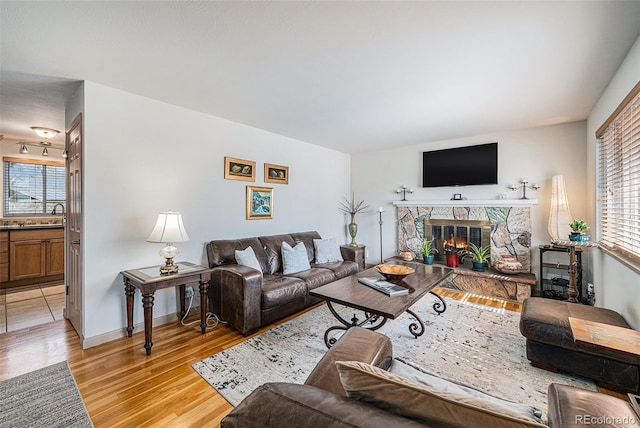 living area featuring light wood finished floors, a stone fireplace, and baseboards