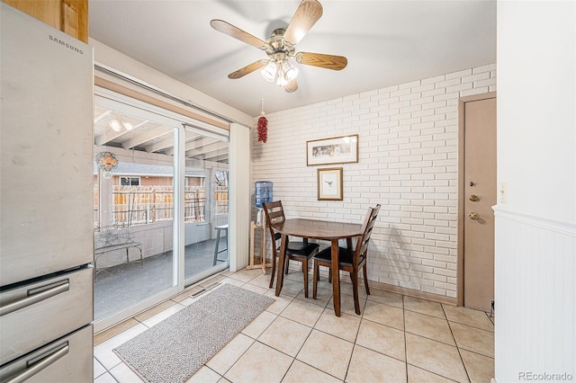 dining space featuring light tile patterned flooring, brick wall, and ceiling fan