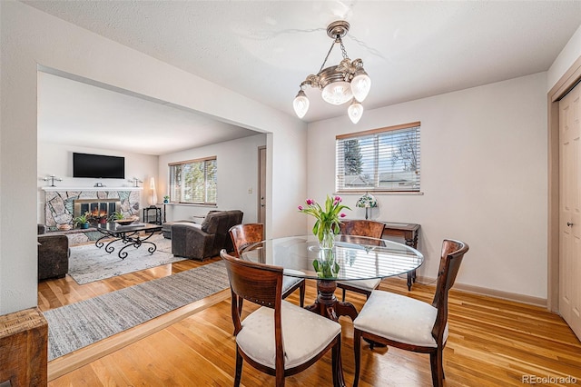 dining room with light wood-type flooring, baseboards, a chandelier, and a fireplace