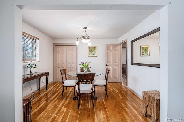 dining area with light wood-type flooring, baseboards, and a notable chandelier