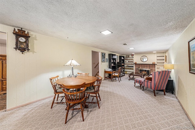 dining space with a textured ceiling, a fireplace, carpet flooring, and wood walls