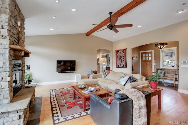 living room featuring wood-type flooring, lofted ceiling with beams, a stone fireplace, and ceiling fan