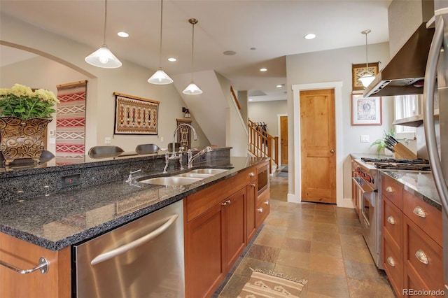 kitchen featuring appliances with stainless steel finishes, dark stone counters, sink, decorative light fixtures, and range hood