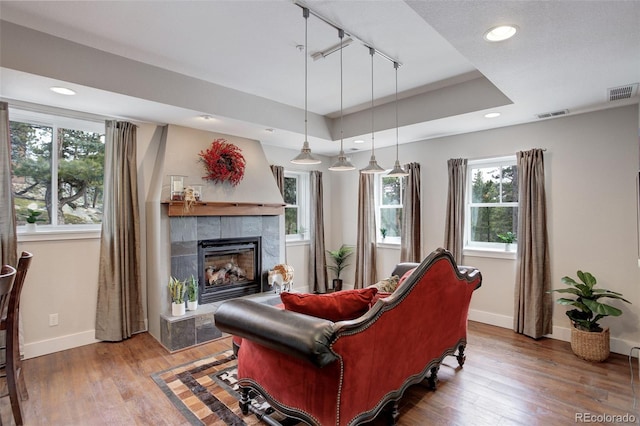 living room featuring hardwood / wood-style flooring, a raised ceiling, a tile fireplace, and track lighting