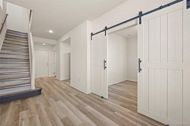 interior space featuring light wood finished floors, a barn door, stairway, and baseboards