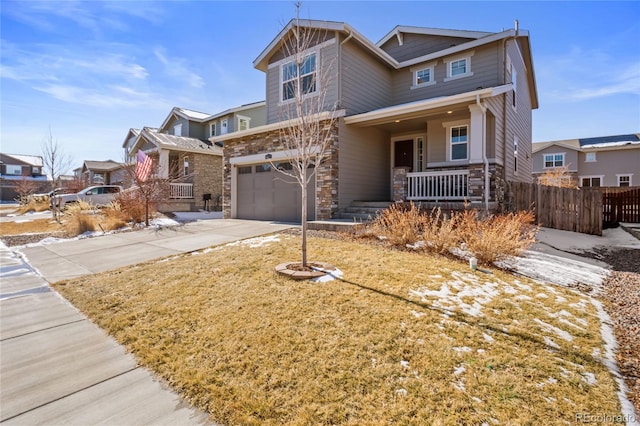 craftsman-style house with covered porch, concrete driveway, fence, a garage, and stone siding