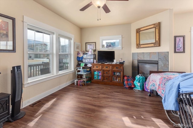 bedroom with a tile fireplace, visible vents, baseboards, and wood finished floors