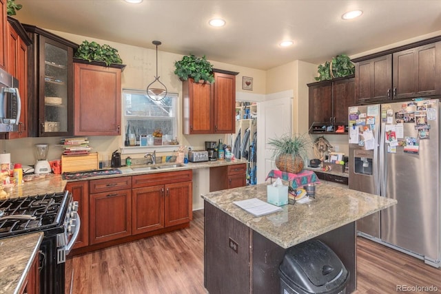 kitchen featuring a sink, hanging light fixtures, light stone countertops, light wood finished floors, and stainless steel fridge