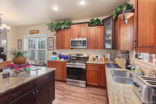 kitchen with stainless steel appliances, glass insert cabinets, a sink, light stone countertops, and light wood-type flooring