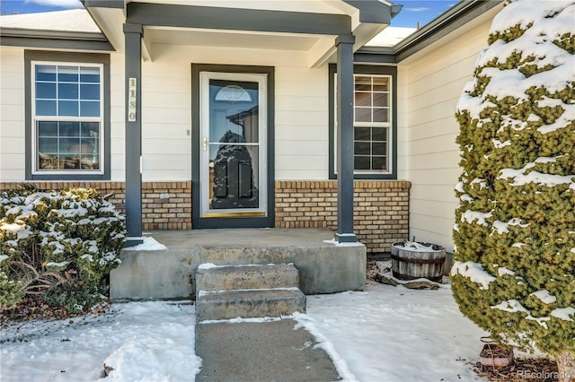 snow covered property entrance with a porch and brick siding
