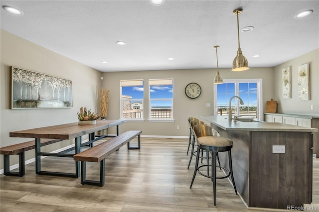 kitchen with baseboards, a sink, light wood-style flooring, and a kitchen island with sink