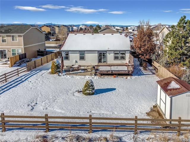 snow covered house featuring an outdoor structure, a deck, a fenced backyard, a storage shed, and a residential view
