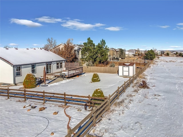 snowy yard with a storage unit, a fenced backyard, an outbuilding, and a deck
