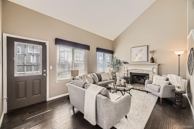 living room featuring dark wood finished floors, a fireplace with raised hearth, baseboards, and high vaulted ceiling