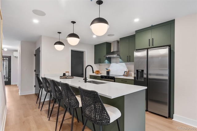 kitchen featuring wall chimney exhaust hood, decorative light fixtures, stainless steel fridge with ice dispenser, green cabinetry, and a breakfast bar area