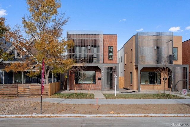 view of front facade with a balcony, fence, and brick siding