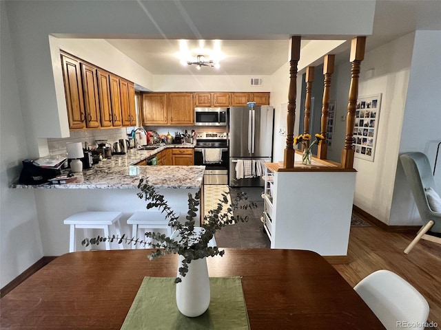 kitchen with a peninsula, a sink, appliances with stainless steel finishes, backsplash, and brown cabinetry