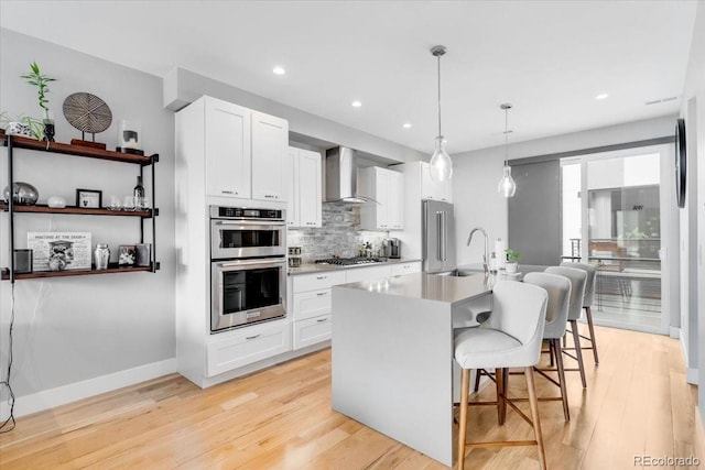 3103 W 18th Ave, Denver, CO 80204 - kitchen with stainless steel appliances, wall chimney exhaust hood, light wood finished floors, tasteful backsplash, and white cabinetry