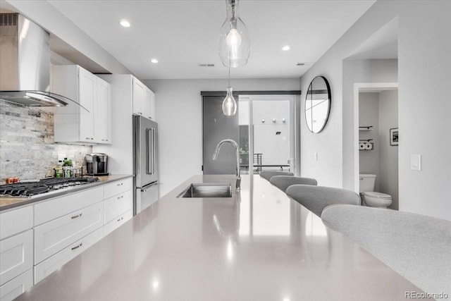3103 W 18th Ave, Denver, CO 80204 - kitchen featuring stainless steel appliances, wall chimney range hood, decorative backsplash, white cabinets, and hanging light fixtures