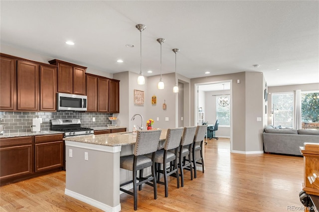 9904 Quintero St, Commerce City, CO 80022 - kitchen with stainless steel appliances, light stone counters, light wood finished floors, decorative backsplash, and a breakfast bar area