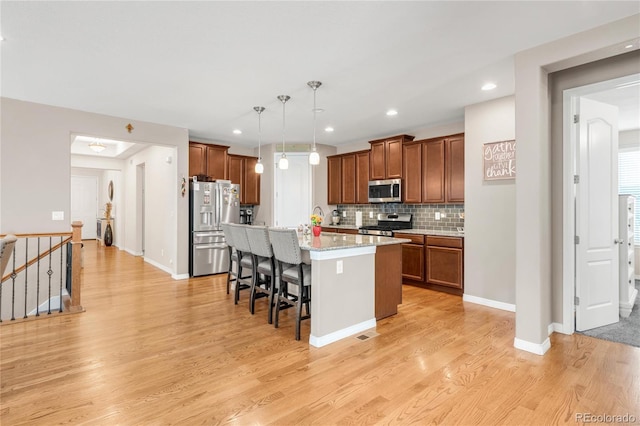 9904 Quintero St, Commerce City, CO 80022 - kitchen featuring appliances with stainless steel finishes, a kitchen breakfast bar, brown cabinets, light wood finished floors, and decorative backsplash