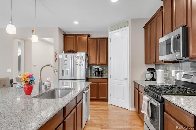 9904 Quintero St, Commerce City, CO 80022 - kitchen with appliances with stainless steel finishes, brown cabinetry, light wood-style floors, tasteful backsplash, and decorative light fixtures