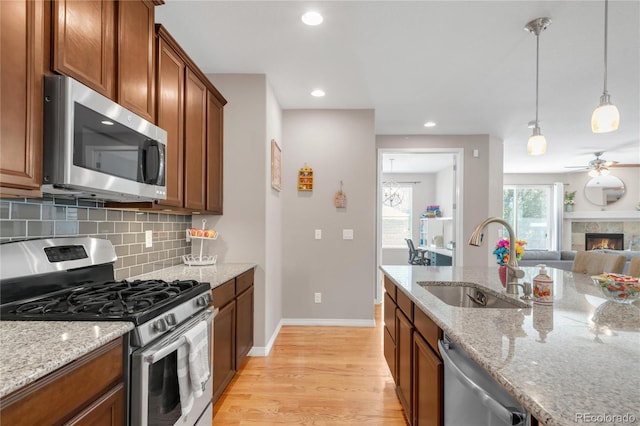 9904 Quintero St, Commerce City, CO 80022 - kitchen featuring stainless steel appliances, decorative backsplash, light wood-style flooring, open floor plan, and light stone countertops