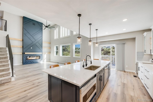 kitchen featuring light wood finished floors, white cabinetry, a sink, a glass covered fireplace, and stainless steel microwave