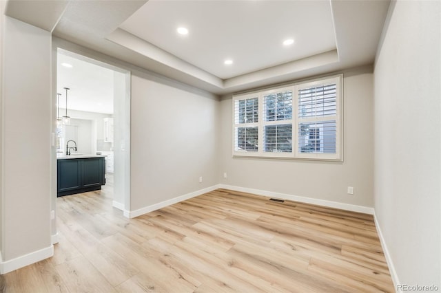 spare room with a sink, a tray ceiling, baseboards, and light wood finished floors