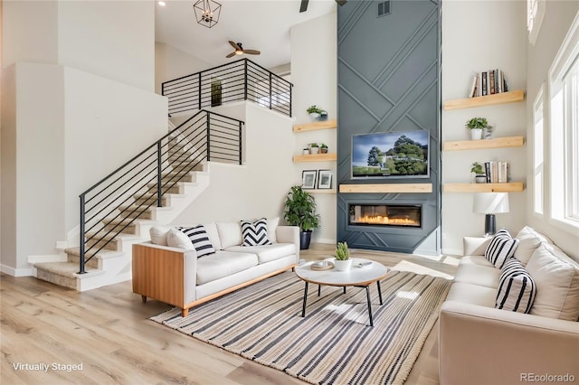 living room with visible vents, wood finished floors, a large fireplace, a high ceiling, and stairs