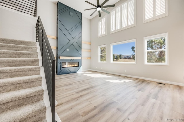 stairway with wood finished floors, baseboards, a high ceiling, ceiling fan, and a large fireplace