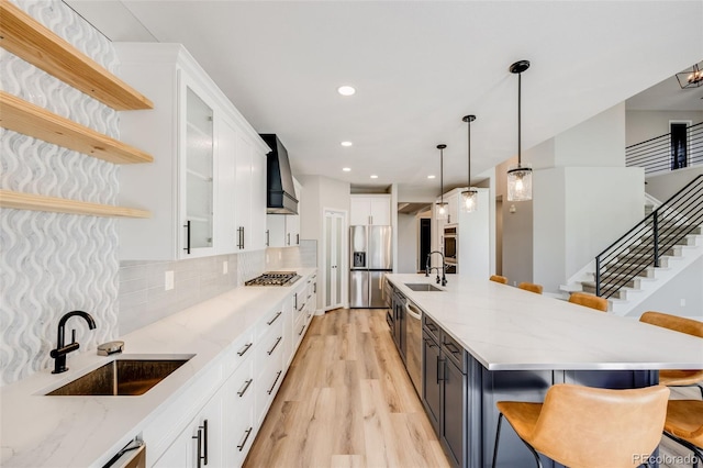 kitchen with light wood-type flooring, stainless steel appliances, custom exhaust hood, white cabinetry, and a sink