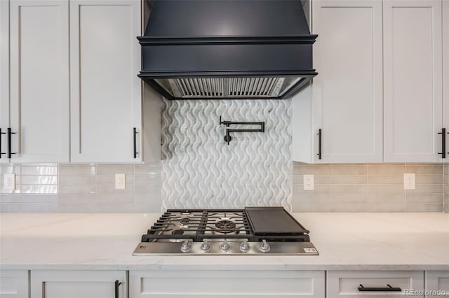 kitchen featuring light stone countertops, premium range hood, stainless steel gas stovetop, white cabinets, and backsplash