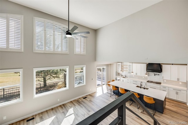 interior space featuring light wood-style flooring, baseboards, a towering ceiling, and a ceiling fan