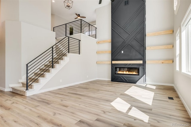 unfurnished living room with baseboards, a large fireplace, a high ceiling, and wood finished floors