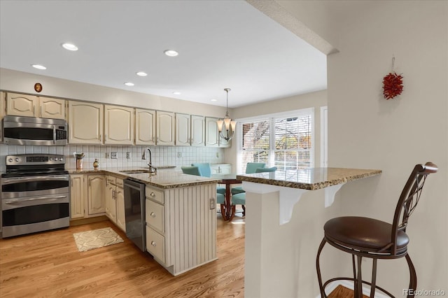 kitchen featuring stainless steel appliances, light stone countertops, light hardwood / wood-style floors, and kitchen peninsula