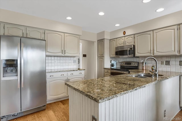 kitchen with stainless steel appliances, light wood-type flooring, sink, dark stone countertops, and kitchen peninsula